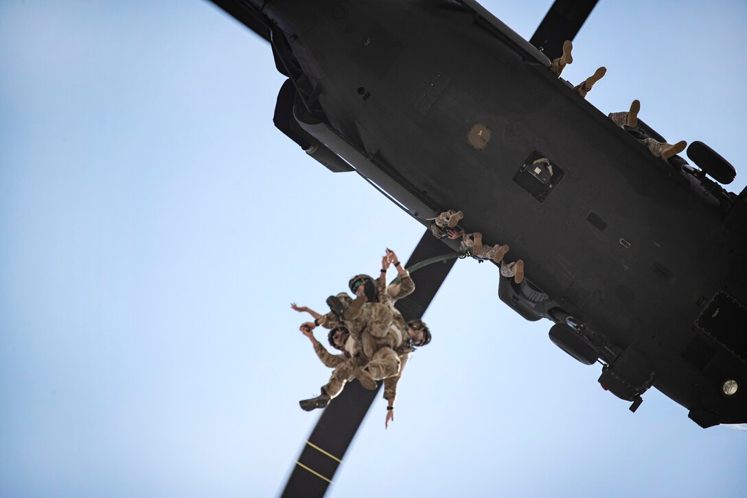 Air Force airmen are raised up underneath a helicopter during a special extraction system demonstration.