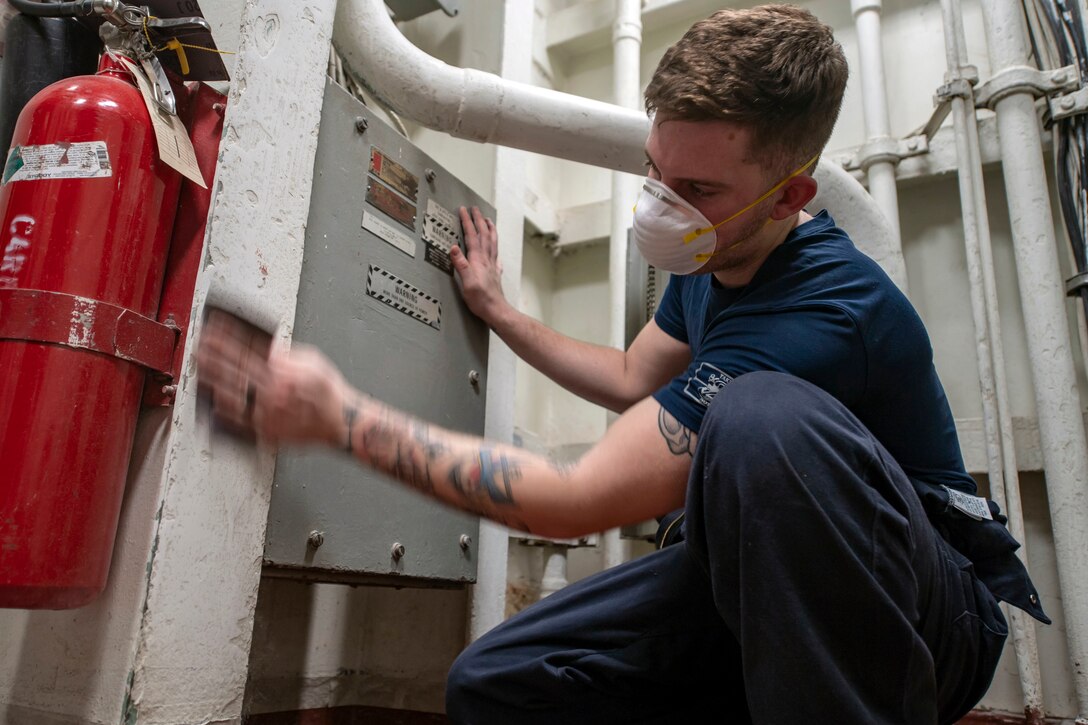 A sailor removes paint from a wall on the USS Essex.