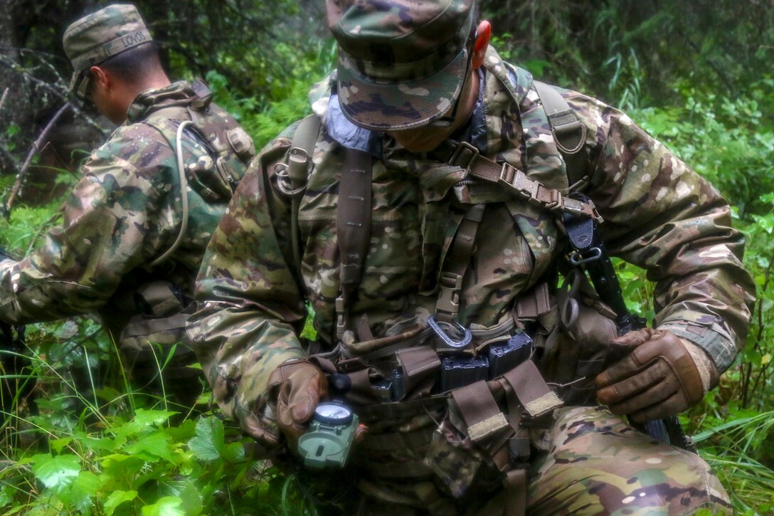 A soldier uses a compass in the woods.