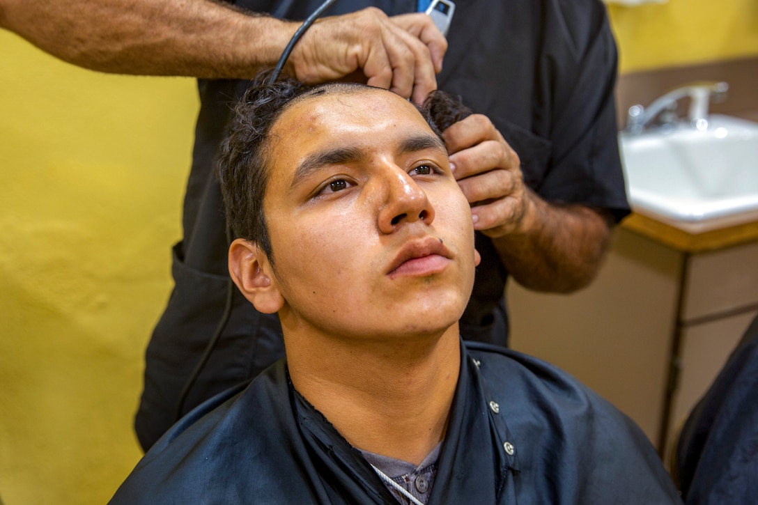 A barber shaves a new recruit's hair.