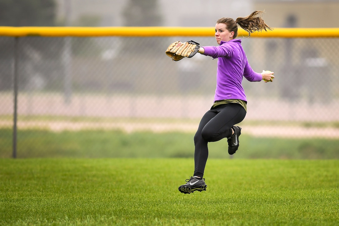 A player in purple leaps and throws a softball.
