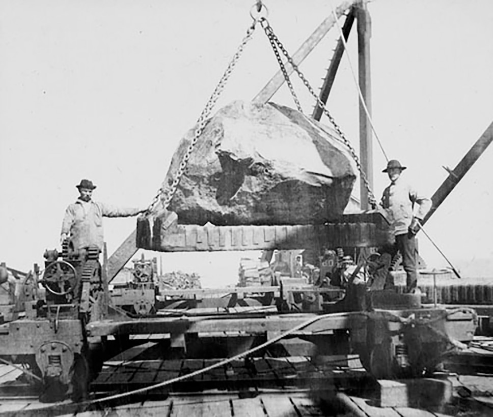 Two workers move a massive stone used in the construction of the South Jetty at the Mouth of the Columbia River in the late 1800s.