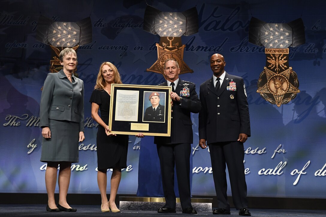 Four people standing in front of a background holding up a memorial plaque.