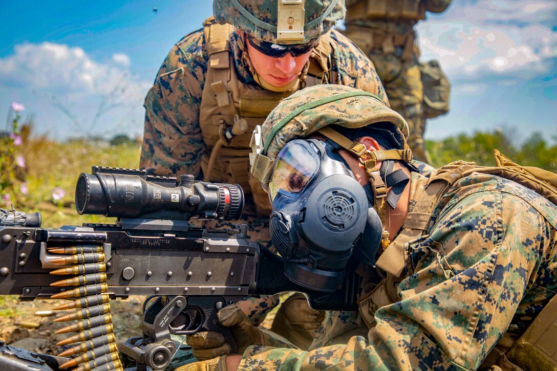 A Marine aims down his weapon while another watches closely.