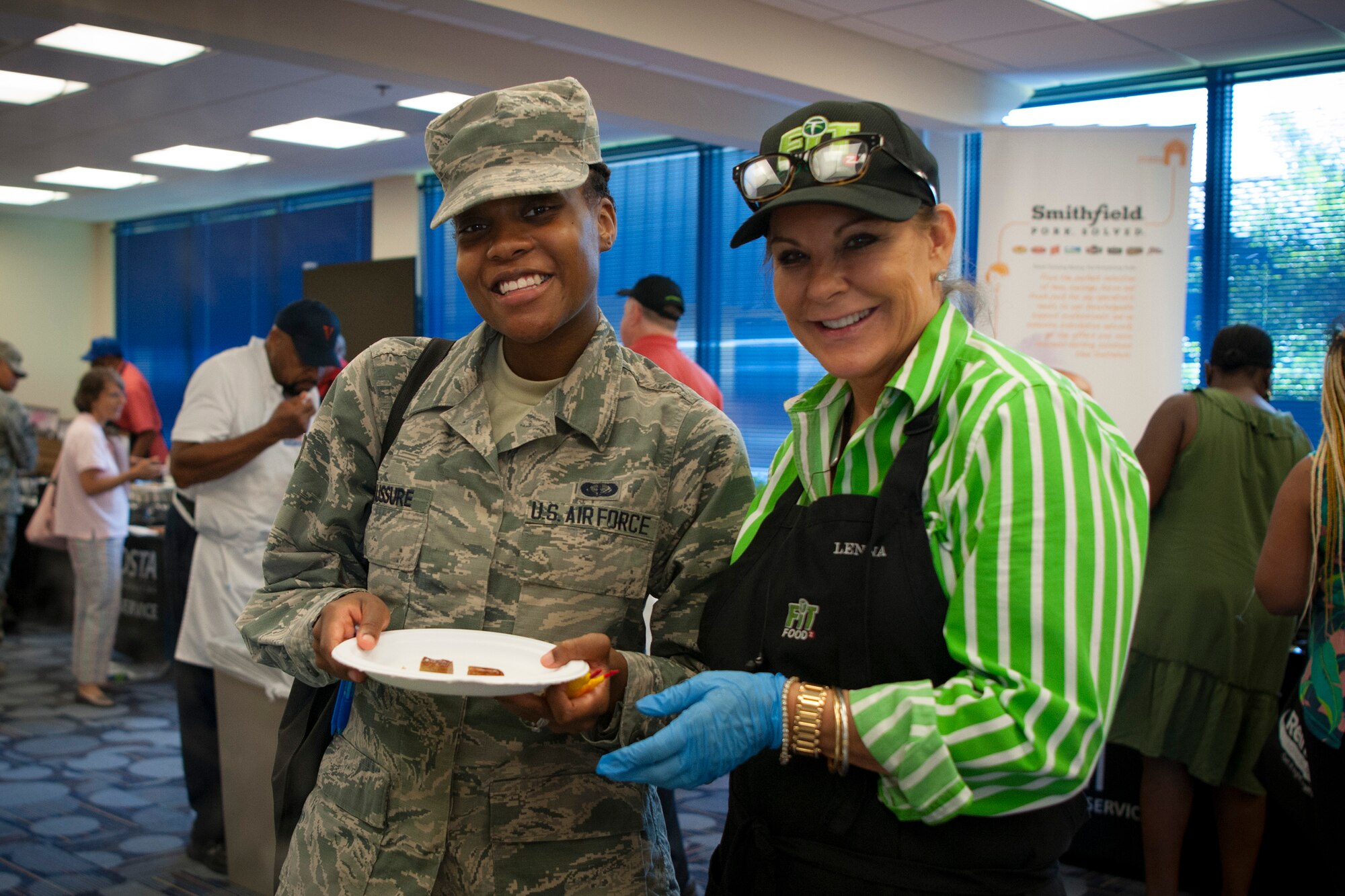 Senior Airman Shania Desaussure, left, 23d Force Support Squadron food service journeyman, and a vendor pose for a photo during the Food Show at the Georgia Pines Dining Facility, Aug. 29, 2018, at Moody Air Force Base, Ga. The Food show is an innovative way to give Airmen an opportunity to try various healthy foods and give feedback. The event allowed the dining facility to focus on incorporating items that meet special dietary needs such as vegan, gluten-free, smoothie bar items and healthy snacks. (U.S. Air Force photo by Airman Taryn Butler)