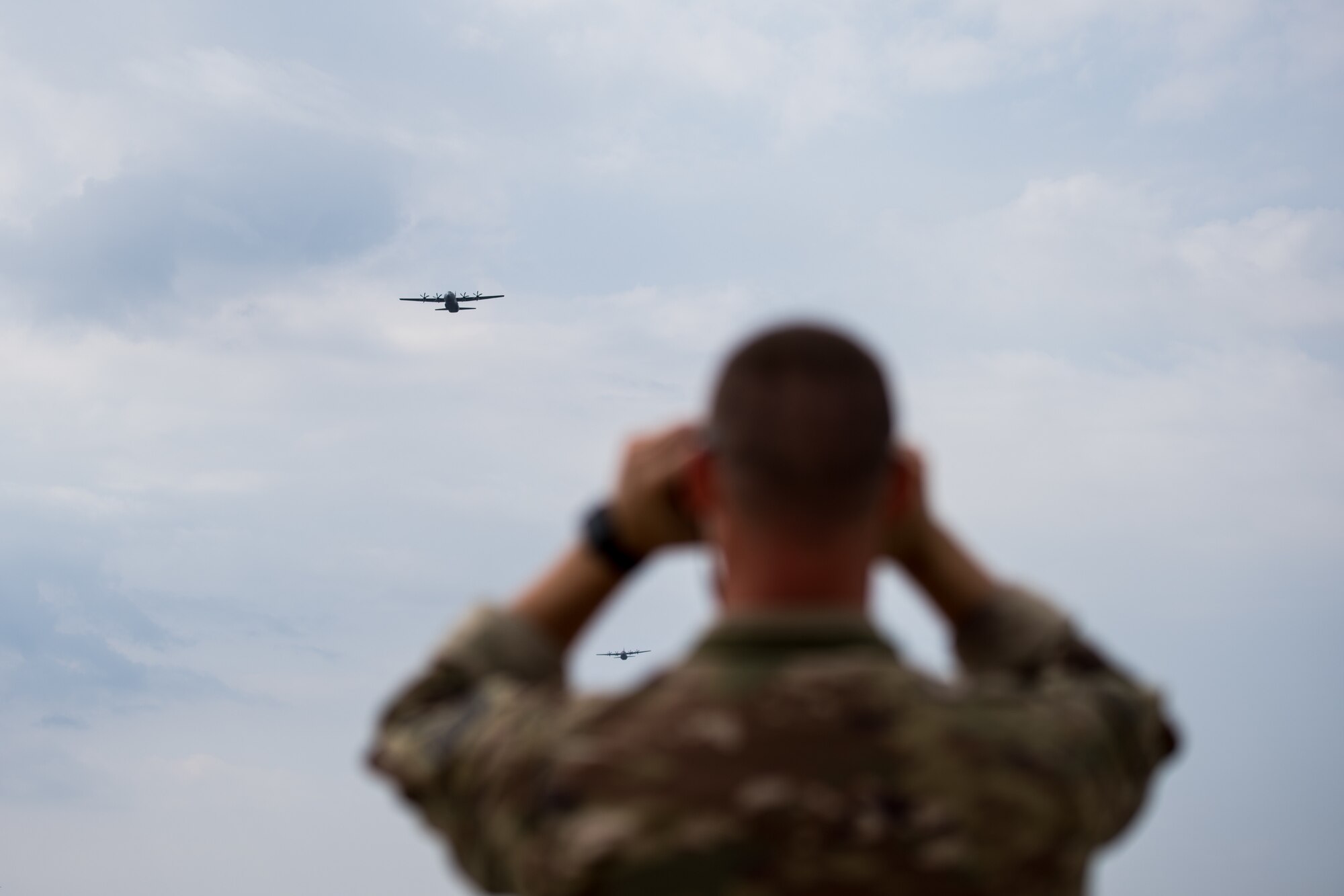 U.S. Air Force Tech. Sgt. Laramie Combs, 435th Contingency Response Squadron contingency airfield manager looks through his binoculars as C-130J Super Hercules aircraft assigned to the 37th Airlift Squadron, Ramstein Air Base, Germany, fly over Boboc Air Base, Romania, Aug. 23, 2018. Combs and his team provided ground support for the 37th AS as part of exercise Carpathian Summer 2018. (U.S. Air Force photo by Senior Airman Devin Boyer)