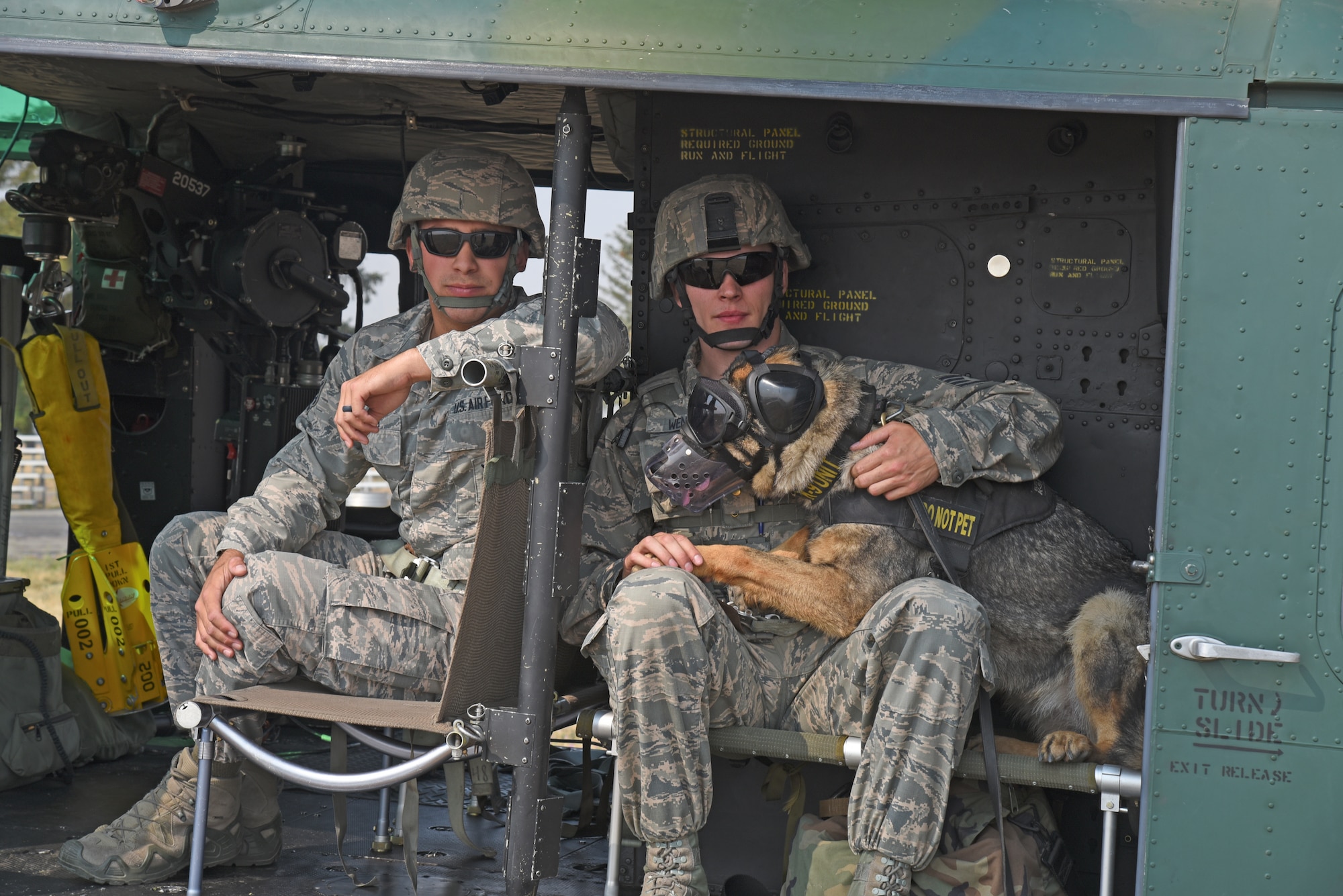 Staff Sgt. Daniel Tabita and Staff Sgt. Kyle Wentz, 92nd Security Forces Squadron Military Working Dog handlers, and MWD Brenda prepare to fly during huey training with the 36th Rescue Squadron Aug. 15, 2018, at Fairchild Air Force Base, Washington. For nearly every dog, it was their first time all four paws have left the ground. For a MWD team, being prepared before heading downrange is imperative to ensuring they meet deployment objectives. (U.S. Air Force photo/Staff Sgt. Mackenzie Mendez)