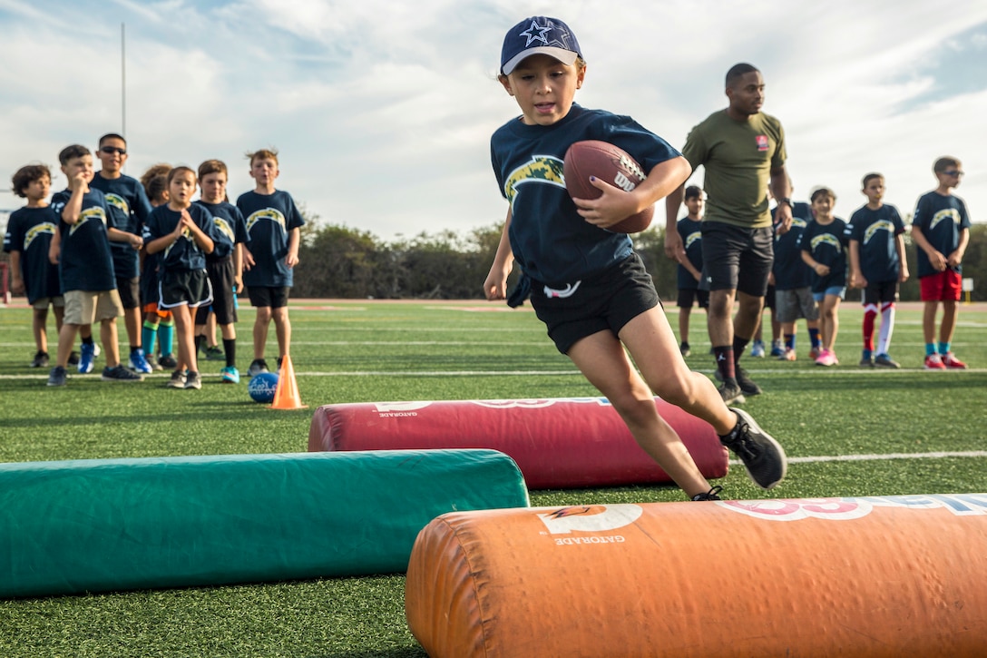 A child runs with a football as others watch on a football field.