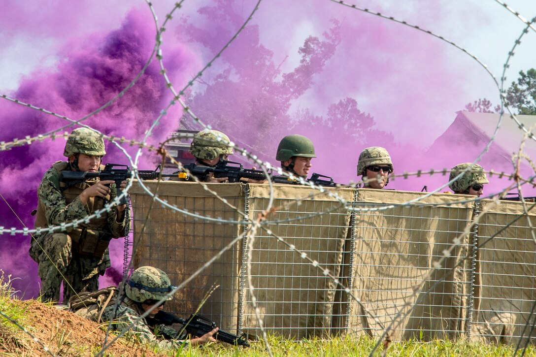 Sailors peek out from behind a barrier as purple smoke billows behind them.