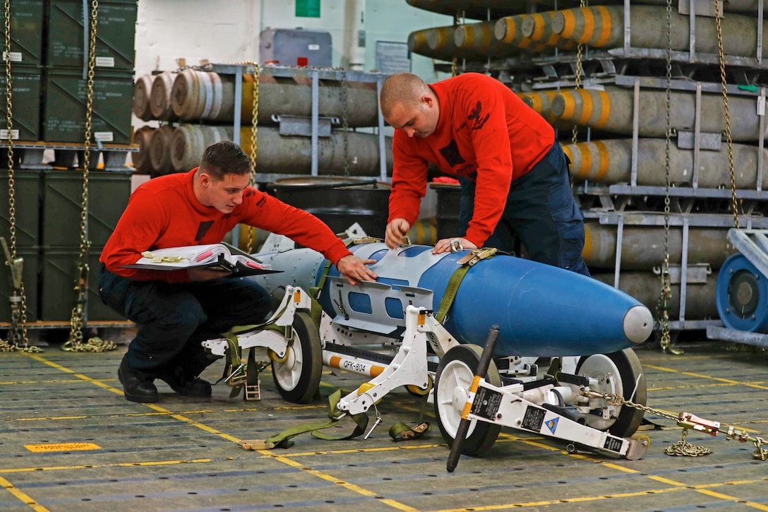 Two sailors examine ordnance on a ship.