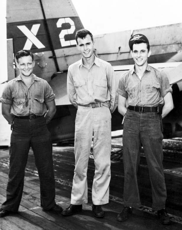 Three WWII-era naval aviators stand in front of their aircraft.
