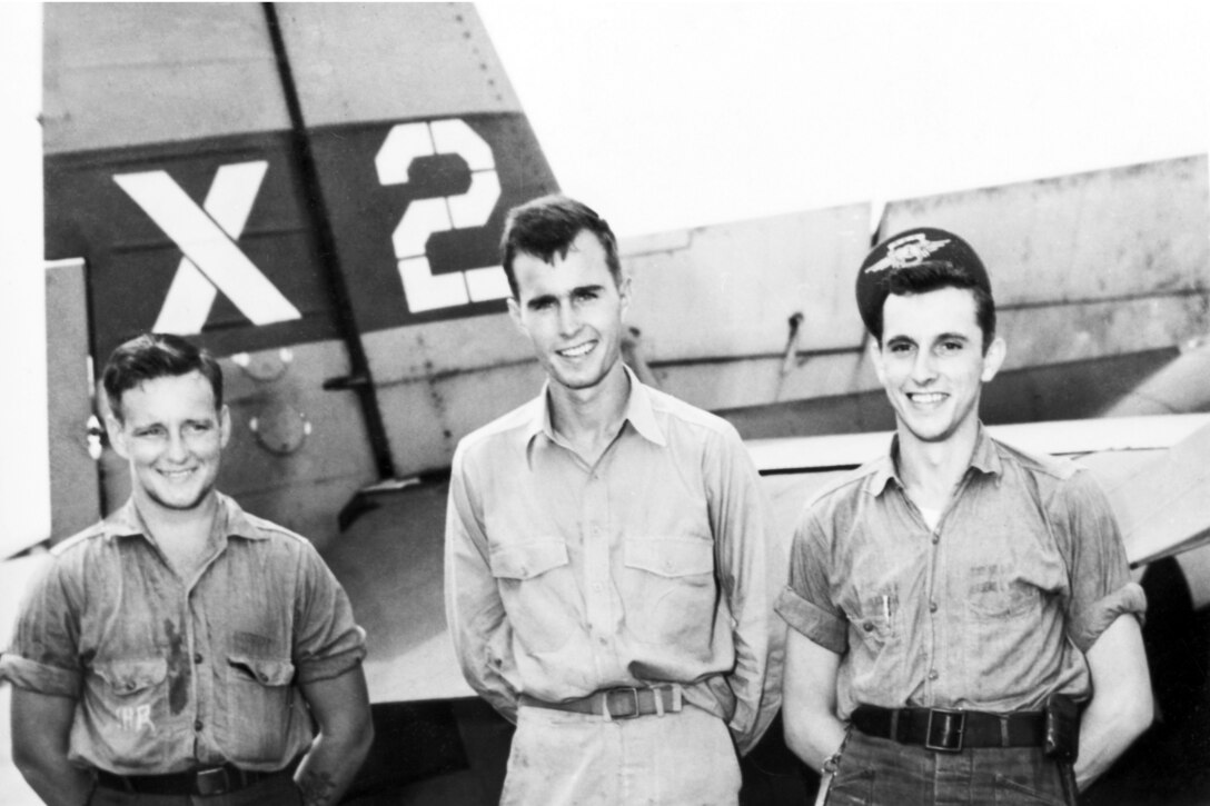 Three WWII-era naval aviators stand in front of their aircraft.