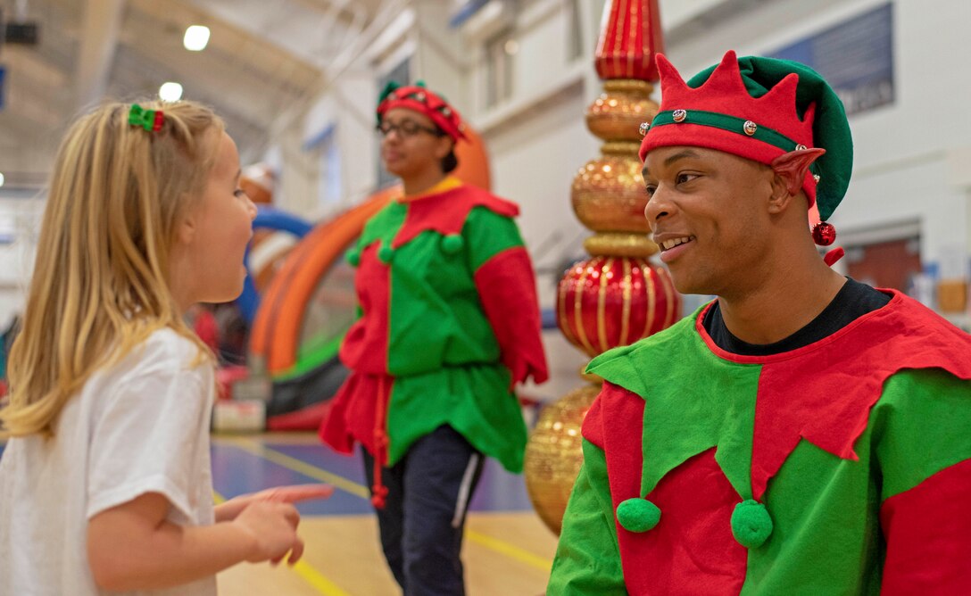 A sailor dressed as an elf talks with a child at a holiday party.