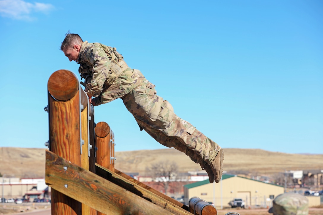 A soldier jumps over a final obstacle on a course.