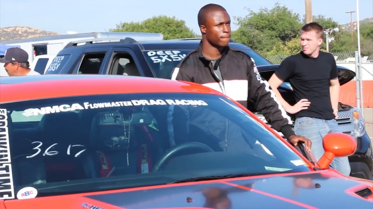 A race car driver stands inside an opened driver’s side door