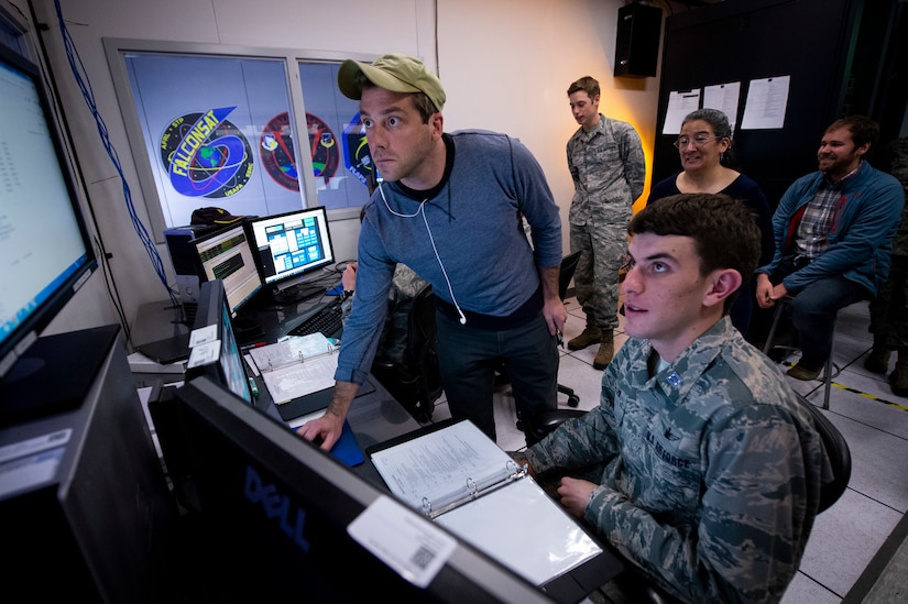 Air Force Academy cadets and civilians look at a computer console.