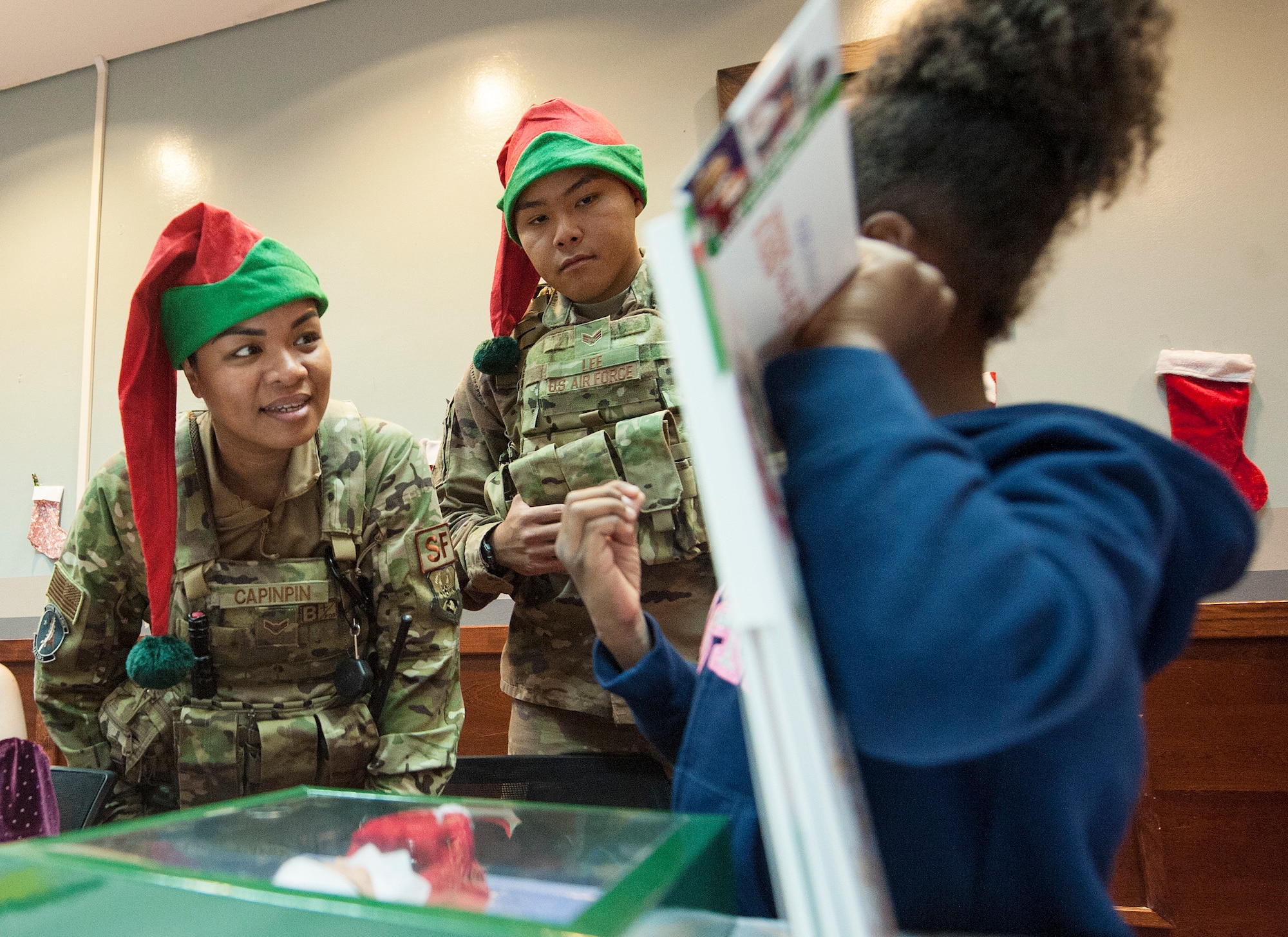 Airman 1st Class Jeannelyn Capinpin, left, and Senior Airman Bronson Lee, both of the 379th Expeditionary Security Forces Squadron, talk to a military child during a holiday kick-off event Dec. 1, 2018, at Al Udeid Air Base, Qatar. Service members and their families were able to play holiday games, watch live music performances, interact with Santa Claus and watch a tree lighting ceremony, during the event. (U.S. Air Force photo by Tech. Sgt. Christopher Hubenthal)