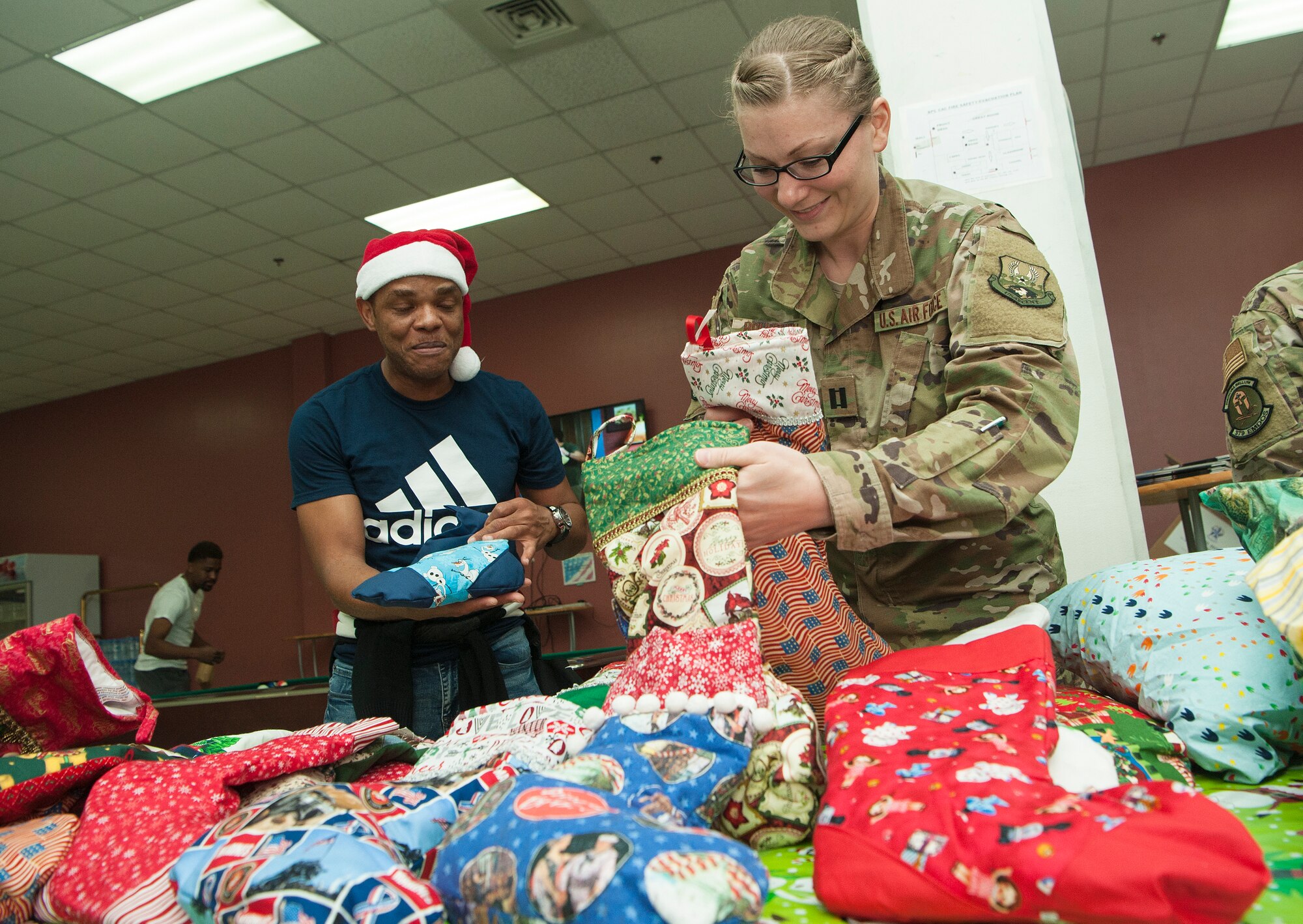 Capt. Beth Brustuen, right, 379th Expeditionary Medical Group mental health clinic officer-in-charge, and Capt. Victor Eguaibor, 379th EMDG mental health clinic licensed social worker, hand out stockings to service members and their families during a holiday kick-off event Dec. 1, 2018, at Al Udeid Air Base, Qatar. Service members and their families were able to play holiday games, watch live music performances, interact with Santa Claus and watch a tree lighting ceremony, during the event. (U.S. Air Force photo by Tech. Sgt. Christopher Hubenthal)