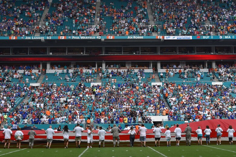 Airmen and local community members unfurl the flag for the National Anthem prior to the start of a Miami Dolphins football game on Dec 2, 2018 in Miami. Approximately 75 Airmen from Patrick Air Force Base, Fla. participated in the event. (U.S. Air Force photo by Tech. Sgt. Andrew Satran)