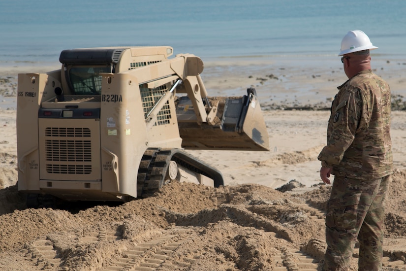 U.S. Army Sgt. Shannon Mapp, right, a heavy equipment operator with B Company, 150th Brigade Engineer Battalion, Mississippi Army National Guard, directs U.S. Army Spc. Laramie Graham, a heavy equipment operator with Bravo Company, 150th BEB, to fill in a ditch created by rainwater runoff at the beach at Kuwait Naval Base, Kuwait, Nov. 30, 2018. The hazard created by the ditch made the beach unsafe for training until the 150th BEB was able to fix it with help from Area Support Group-Kuwait's Directorate of Public Works.