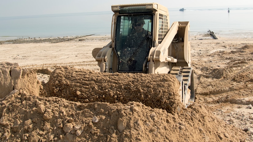 U.S. Army Spc. Laramie Graham, a heavy equipment operator with Bravo Company, 150th Brigade Engineer Battalion, Mississippi Army National Guard, uses a skid-steer to move sand to fill in a ditch formed by rainwater runoff at the beach at Kuwait Naval Base, Kuwait, Nov. 30, 2018. The hazard created by the ditch made the beach unsafe for training until the 150th BEB was able to fix it with help from Area Support Group-Kuwait's Directorate of Public Works.