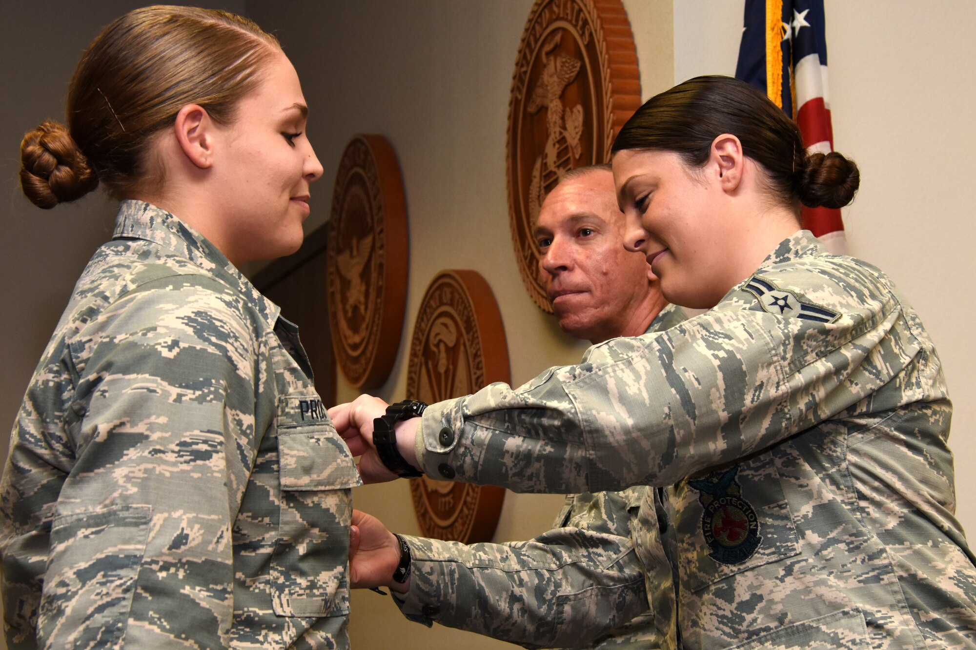 U.S. Air Force Lt. Col. Scott Cline, 312th Training Squadron commander, watches as Airman 1st Class Erin Prosser pins a duty badge onto Airman Emma Prosser at her graduation from the Louis F. Garland Department of Defense Fire Academy on Goodfellow Air Force Base, Texas, Dec. 3, 2018. Erin and Emma Prosser are twins, Erin joined the Air Force shortly before her sister and graduated the fire academy in March of 2018. (U.S. Air Force photo by Airman 1st Class Seraiah Hines/Released