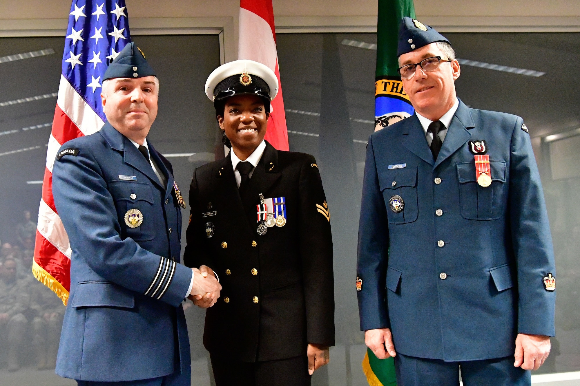 Royal Canadian Navy Master Seaman Malisa Ogunniya (center), Western Air Defense Sector Canadian Detachment chief clerk, is awarded the Canadian Armed Forces Special Service Medal with NATO bar from Lt. Col. Michael Fawcett, WADS Canadian Detachment commander (left), Dec. 1, 2018 at Joint Base Lewis-McChord, Washington.  The medal was awarded for Ogunniya’s exceptional service in support of operations while onboard Her Majesty’s Canadian Ship Winnipeg from July 2015 through January 2016.  HMCS Winnipeg conducted operations under the standing NATO Maritime Group Two as part of Operation Reassurance, NATO’s mission to build maritime situational awareness in order to detect, deter and disrupt terrorism in the Mediterranean Sea. The Special Service Medal was created to recognize members of the Canadian Armed Forces who have performed a service determined to be under exceptional circumstances, in a clearly defined locality for a specified duration.  The SSM is always issued with a bar that specifies the special service being recognized, each bar having its own criteria. (U.S. Air National Guard photo by Maj. Kimberly D. Burke)