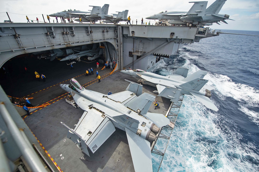Sailors direct F/A-18E Super Hornets onto an aircraft elevator aboard an aircraft carrier.