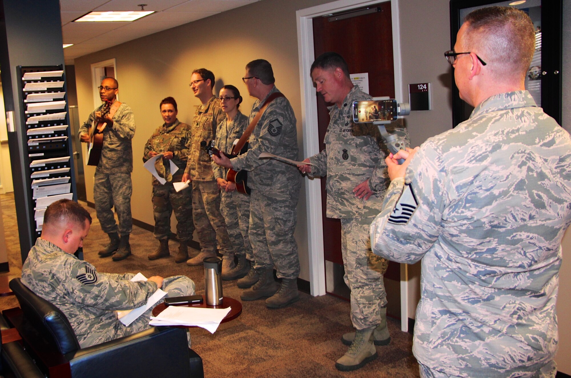 Col. Lance Turner, the 932nd Mission Support Group's multi-talented commander, along with other officers and enlisted leadership, stopped by the 932nd Force Support Squadron customer service waiting room to share in some holiday song Dec 2, 2018, at Scott Air Force Base, Illinois.  They sang various songs during the Unit Training Assembly to help Airmen pass the time in the line.  The other talented guitar player, third from the right, is Master Sgt. Tony Loving, and all the action was captured for historical documentation by Master Sgt. Christopher Parr on his tripod and video camera combo at far right.  (U.S. Air Force photo by Lt. Col. Stan Paregien)