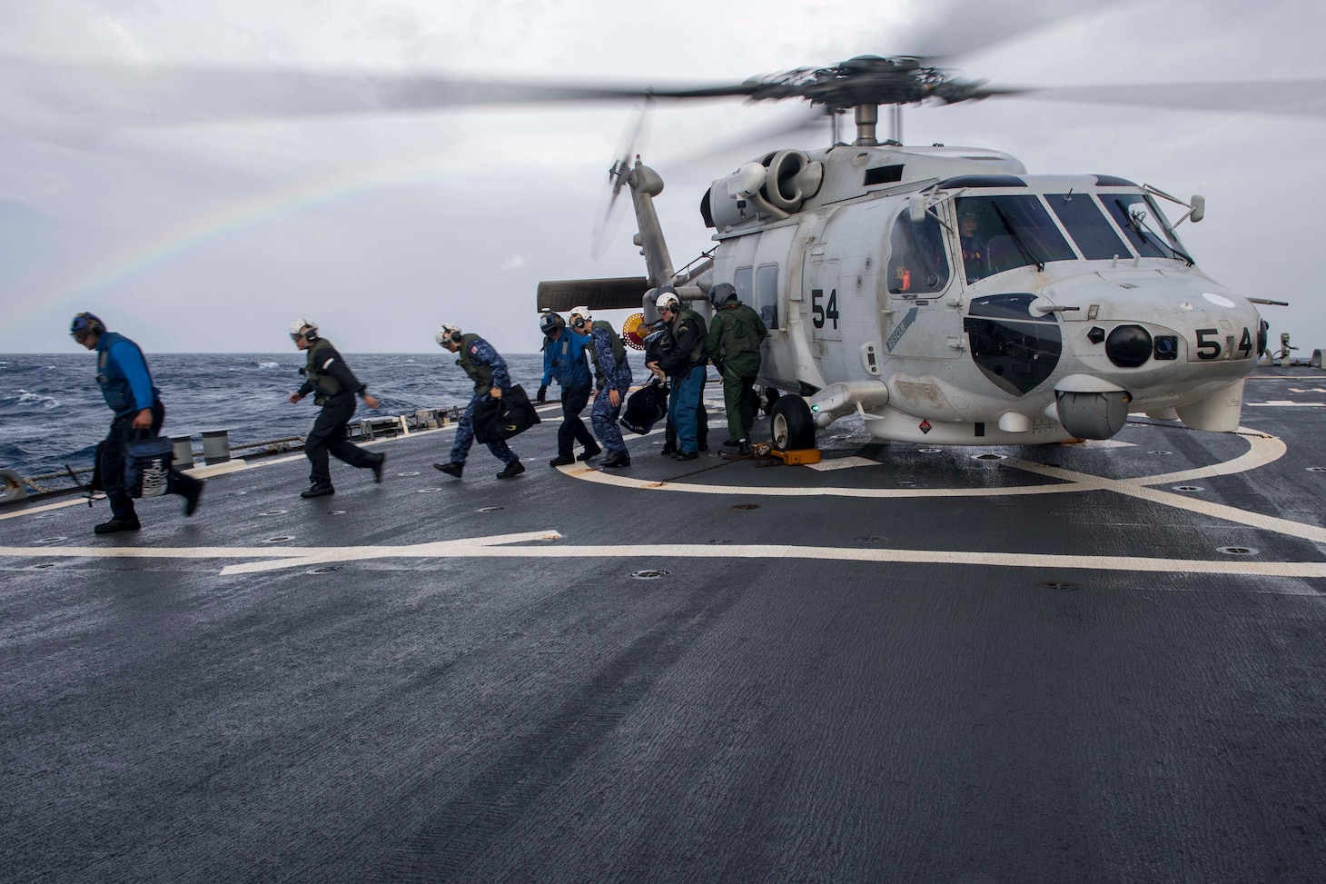 WATERS SOUTH OF JAPAN (Dec. 4, 2018) Japan Maritime Self-Defense Force (JMSDF) sailors, assigned to the JMSDF destroyer JS Hyuga (DDH-181), depart a JMSDF MH-60K Sea Hawk helicopter on the flight deck aboard the Arleigh Burke-class guided-missile destroyer USS Benfold (DDG 65). Benfold is forward-deployed to the U.S. 7th Fleet area of operations in support of security and stability in the Indo-Pacific region.