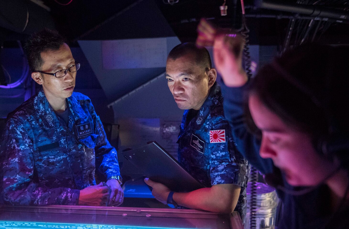 WATERS SOUTH OF JAPAN (Dec. 4, 2018) Japan Maritime Self-Defense Force (JMSDF) sailors assigned to the JMSDF destroyer JS Hyuga (DDH-181), observe as an anti-submarine scenario occurs in the combat information center aboard the Arleigh Burke-class guided-missile destroyer USS Benfold (DDG 65). Benfold is forward-deployed to the U.S. 7th Fleet area of operations in support of security and stability in the Indo-Pacific region.