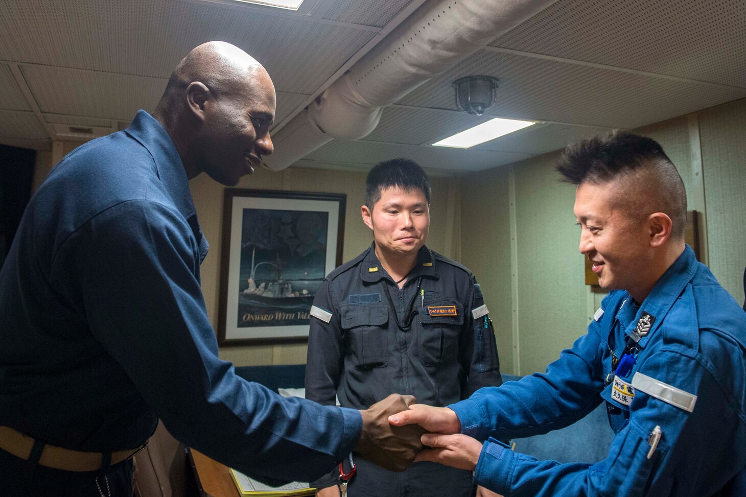 WATERS SOUTH OF JAPAN (Dec. 4, 2018) Cmdr. Leroy Mitchell, commanding officer of the Arleigh Burke-class guided-missile destroyer USS Benfold (DDG 65), greets Japan Maritime Self-Defense Force (JMSDF) Chief Operations Specialist Hideki Okubo, assigned to the JMSDF destroyer JS Hyuga (DDH-181), in the captain’s cabin during a tour aboard Benfold. Benfold is forward-deployed to the U.S. 7th Fleet area of operations in support of security and stability in the Indo-Pacific region.