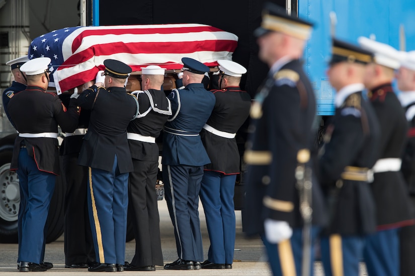 Service members lift a flag-draped coffin into a truck.