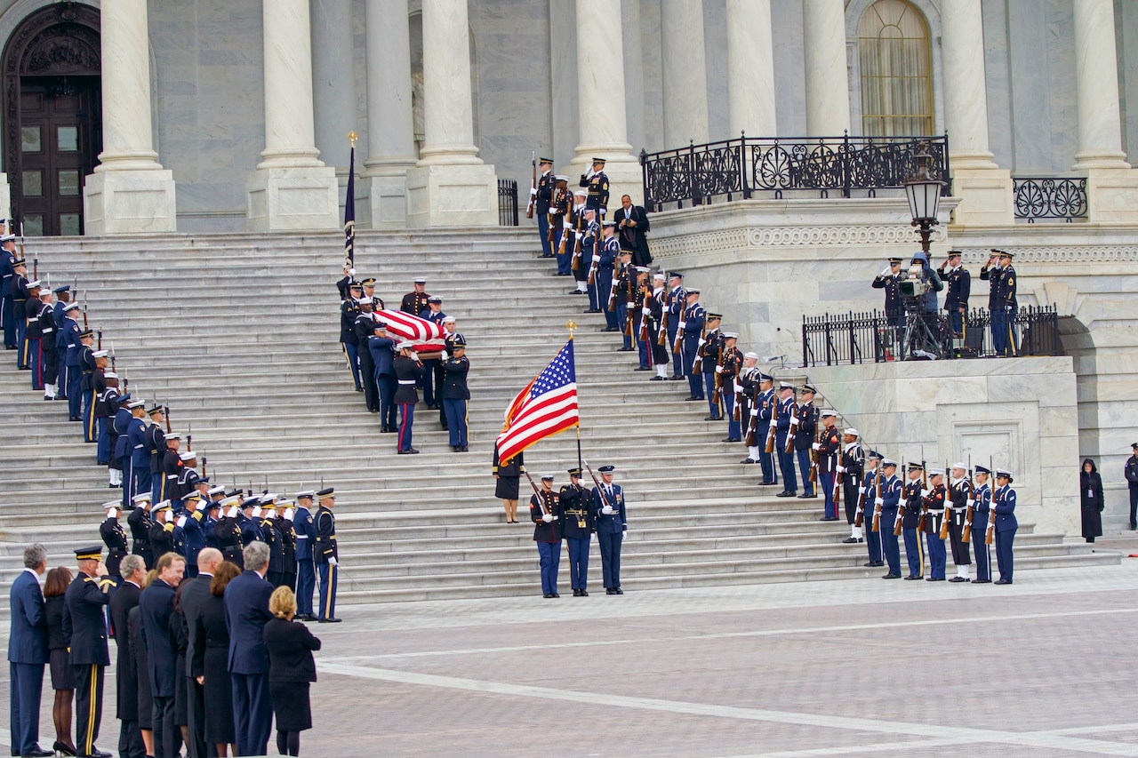 Service members bring a flag-draped coffin down the steps of the U,S, Capitol.