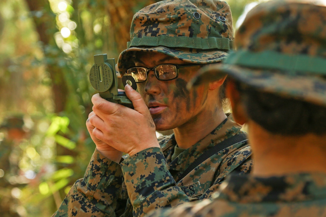 A Marine wearing camouflage looks through a compass.