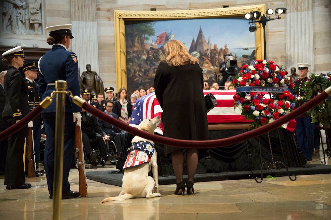Service members, a woman and a service dog stand beside George H.W. Bush's casket at a funeral service