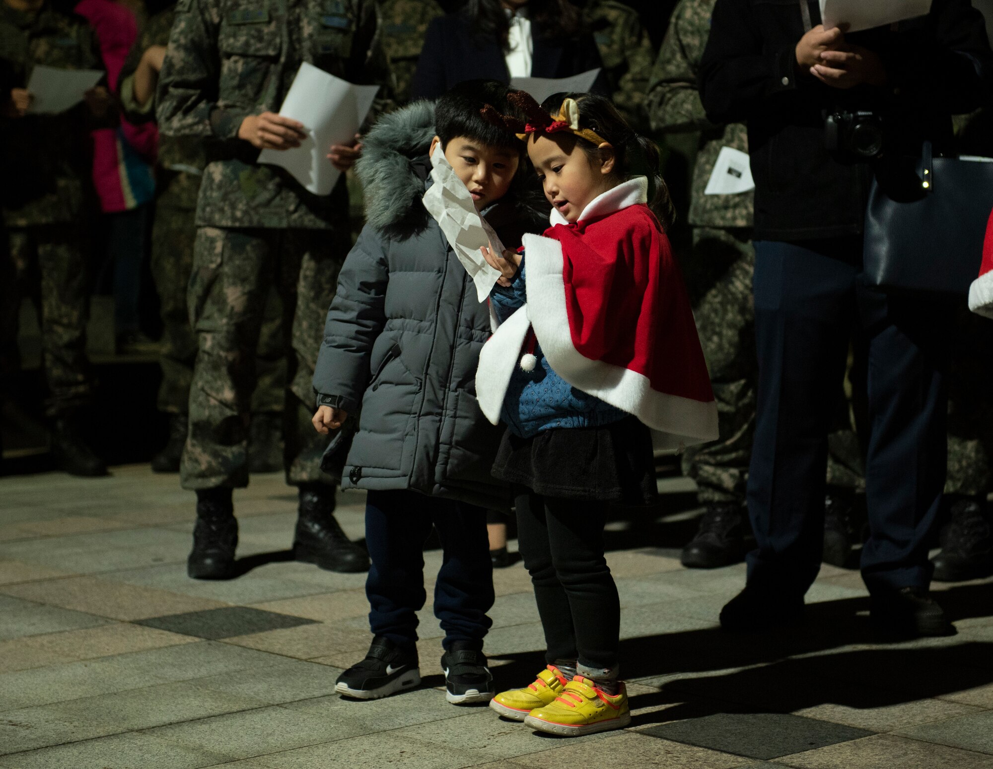 Two Korean children read Christmas carol lyrics at Kunsan Air Base, Republic of Korea, Nov. 29, 2018. The 8th FW chapel held a base-wide event for the Wolf Pack and Republic of Korea Air Force’s 38th Fighter Group to come out and be a part of the tree lighting ceremony. (U.S. Air Force photo by Senior Airman Stefan Alvarez)