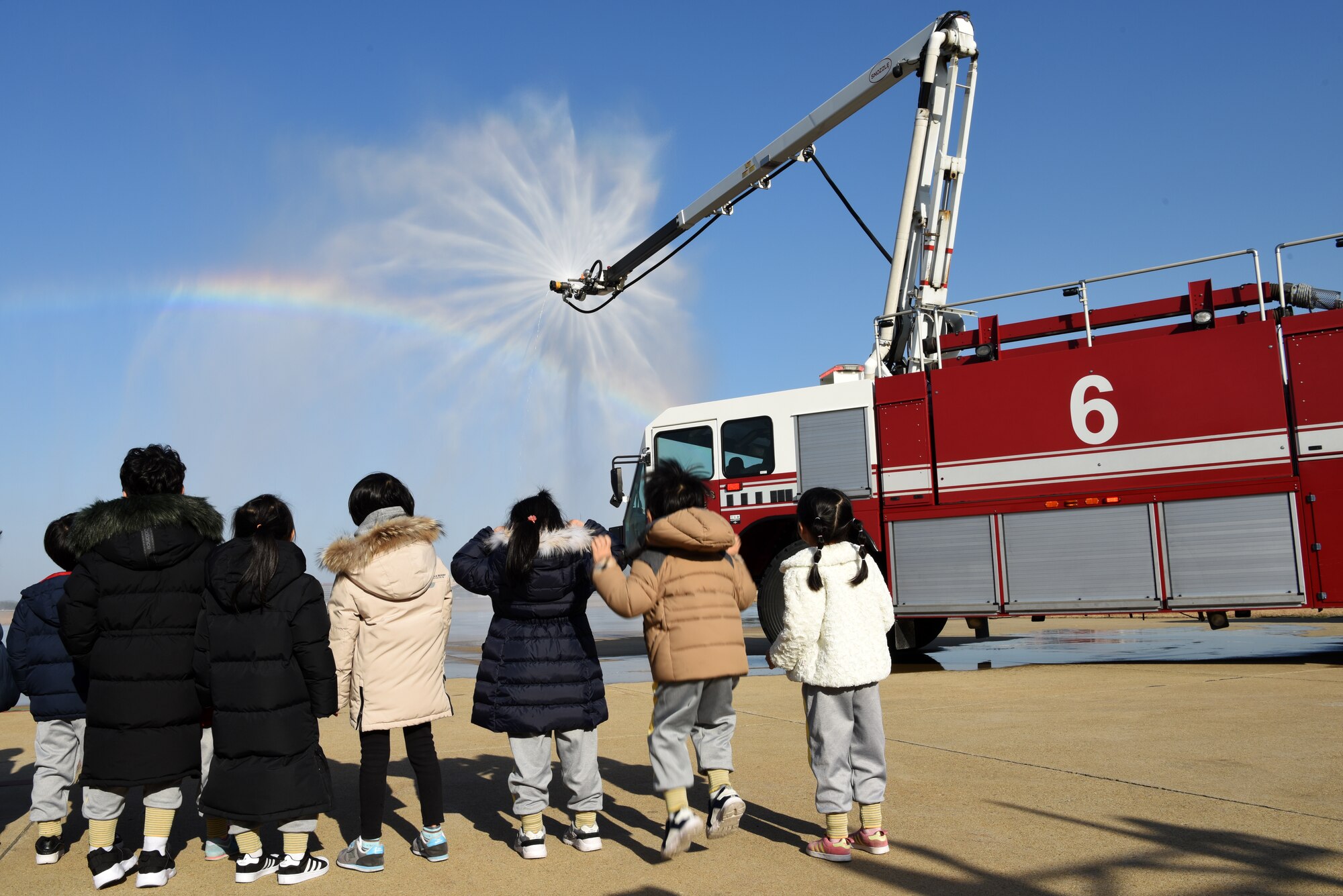 Korean Christian International School students watch a fire truck spray water at Kunsan Air Base, Republic of Korea, Nov. 30, 2018. During the visit, the children toured the 8th Civil Engineer Squadron fire house and met with both Korean and American firefighters. (U.S. Air Force photo by Staff Sgt. Joshua Edwards)