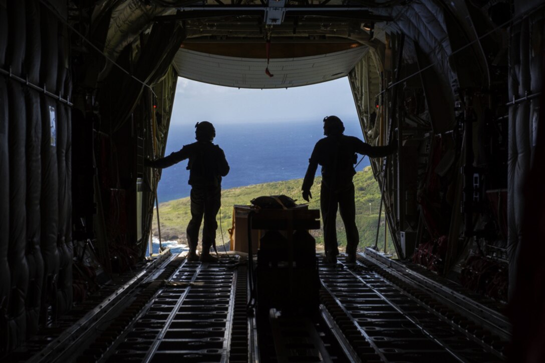 Two service members overlook the ocean in an aircraft ready for a practice drop.