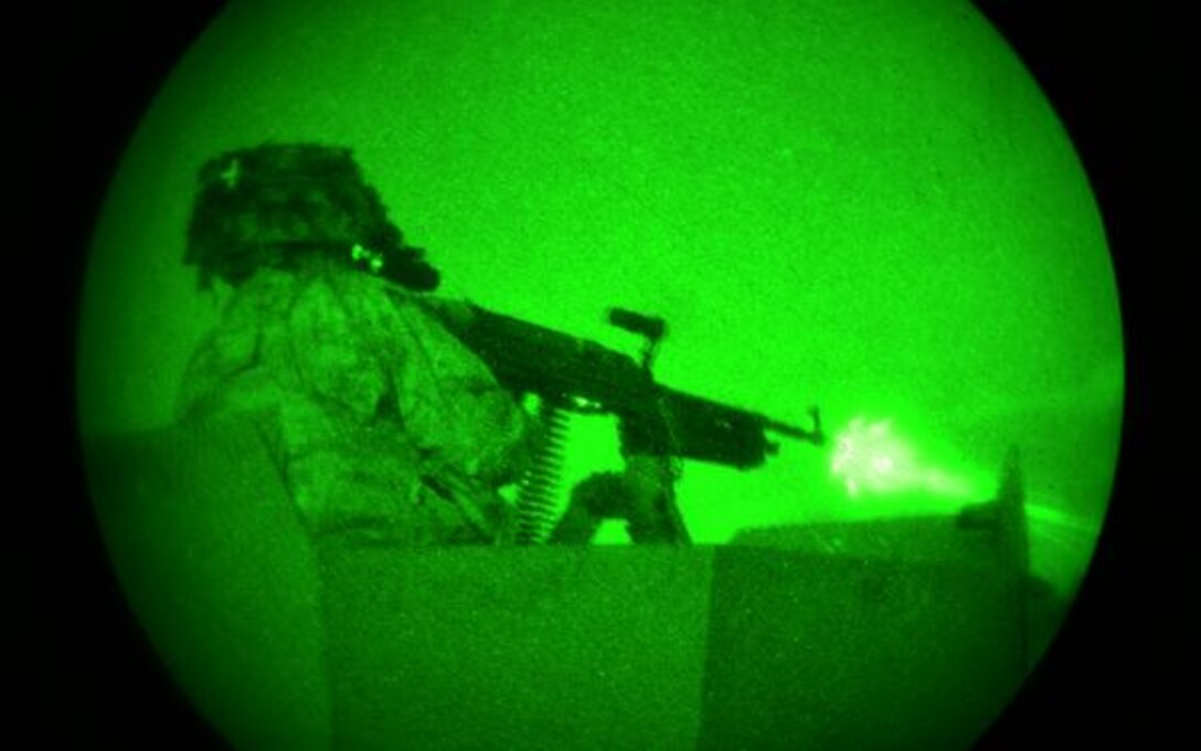 A solider shoots at targets with a machine gun under the night sky.