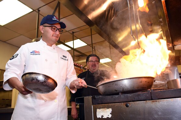 Senior Airman Oscar Callejas, left, 60th Force Support Squadron food service shift worker, pan-fries a skillet of food under the watchful eye of his mentor and friend, Maynard Oestreich, right, Travis Air Force Base executive chef, Dec. 6. Oestreich was among the first of Callejas's leadership to recognize his talent for cooking and was a driving force behind Callejas's now-decorated career. (U.S. Air Force photo by Airman 1st Class Christian Conrad)