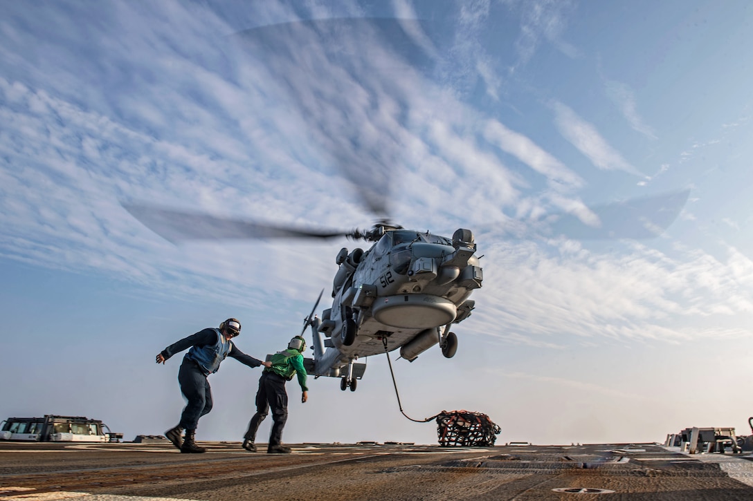 Two sailors move away from a hovering helicopter.