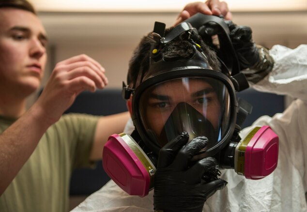 Airman 1st Class Conor Wilson, 375th Aerospace Medicine Squadron bioenvironmental engineering technician, assists Airman William Wang, 375th AMDS BE technician, with donning his gas mask during a training exercise on Nov. 29, 2018, at Scott Air Force Base, Illinois. Wang wears the gas mask to complete his level C protection gear which consists of an air purifying half or full mask respirators, chemical-resistant overalls with a hood, outer and inner chemical-resistant gloves and steel-toe boots.