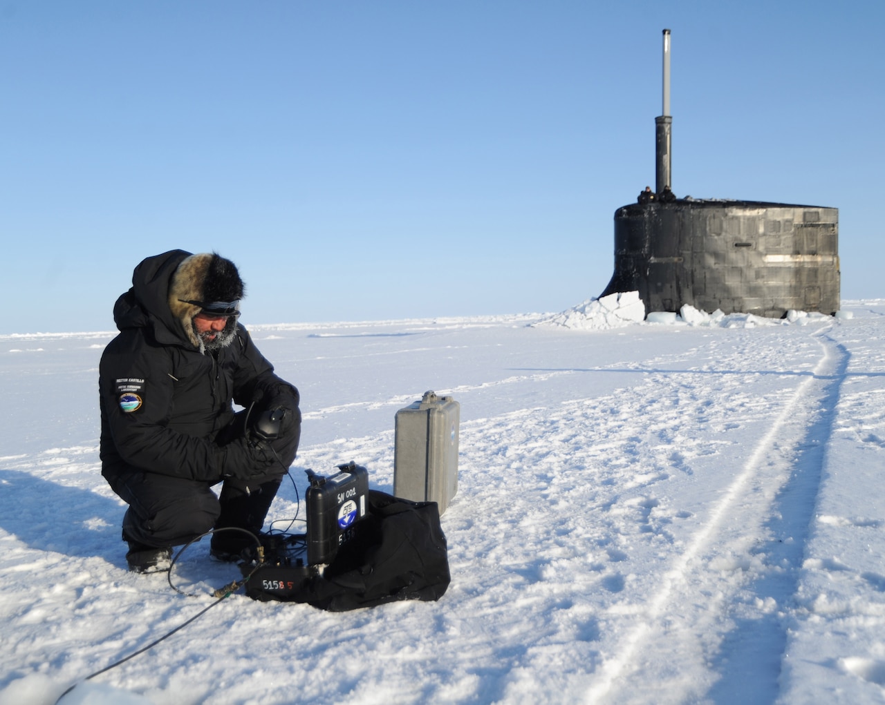 A sailor kneels on ice in front of a submarine.