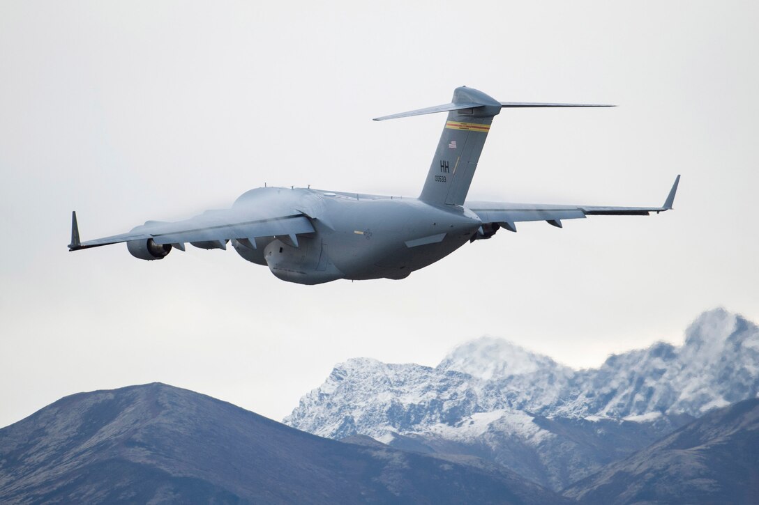 A C-17 Globemaster III flies above snow-capped mountains.