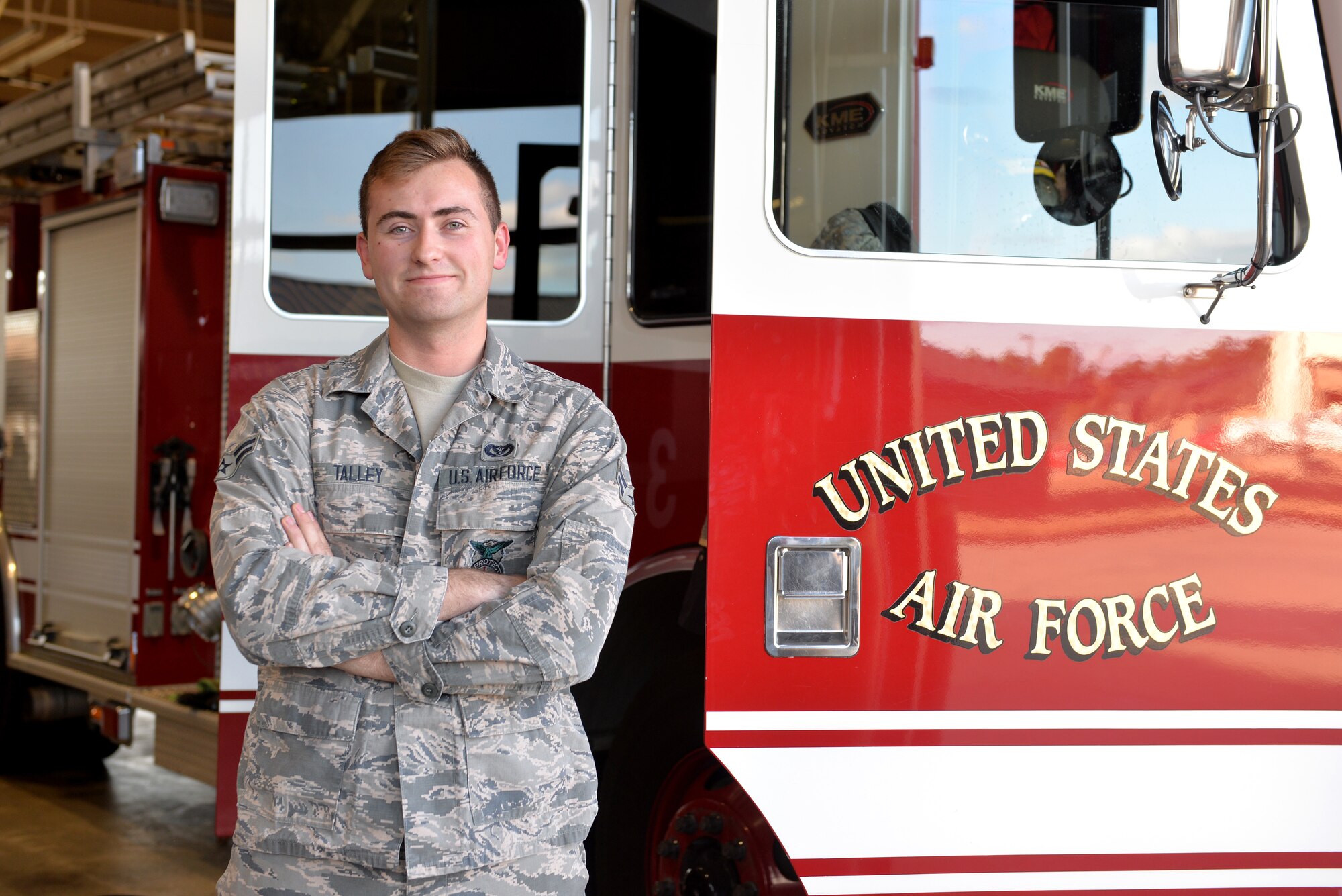 A man wearing the Airman Battle Uniform has his arms folded in front of a firetruck.