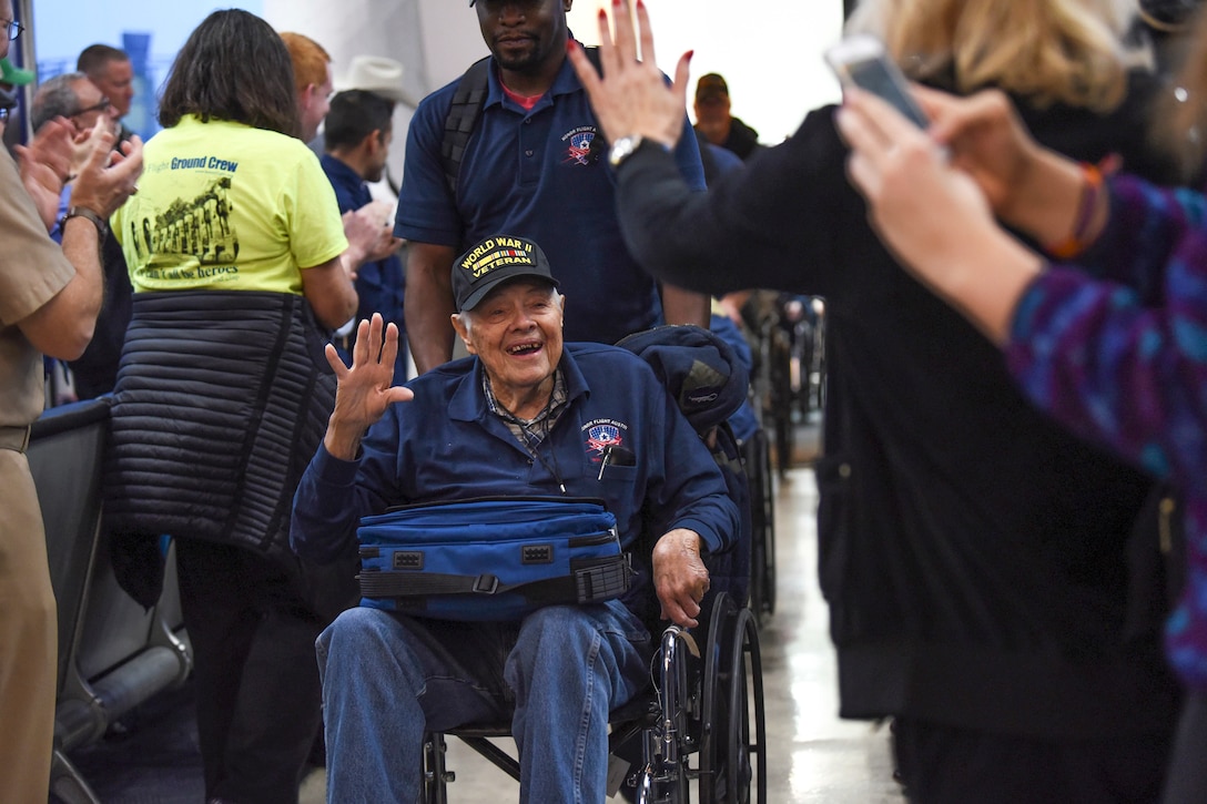 A veteran in a wheelchair smiles and waves to people welcoming him at an airport.