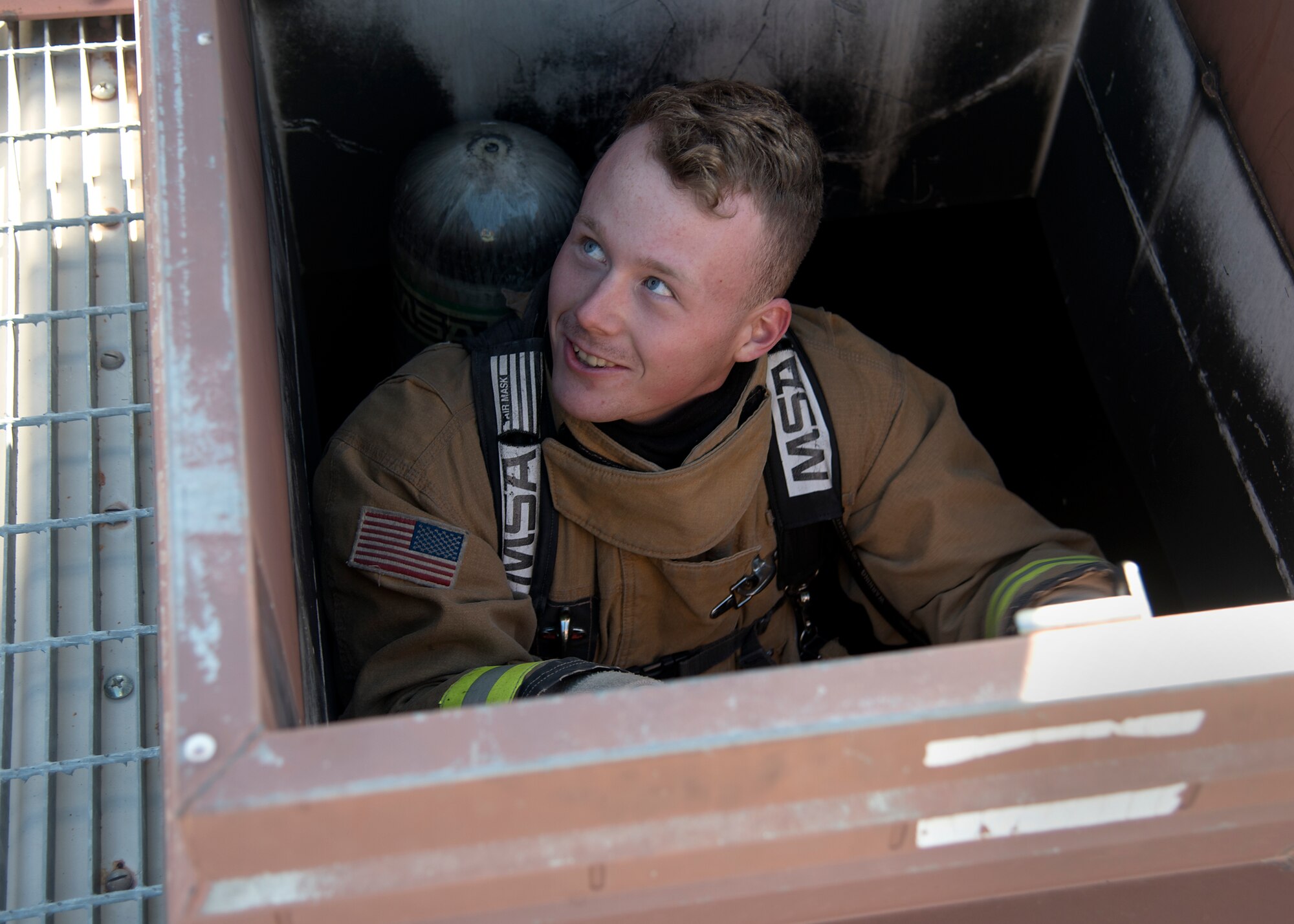 A firefighter climbs up a ladder and through an opening in a roof.