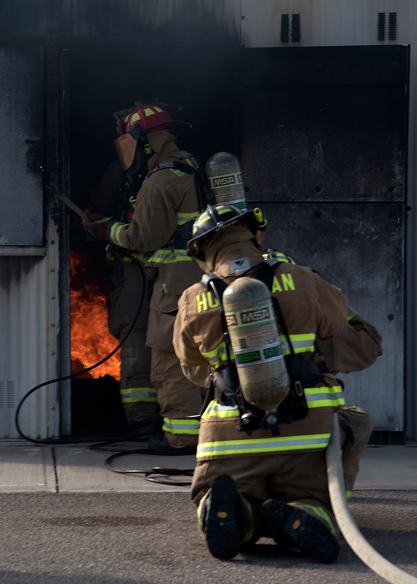 Two firefighters hold a fire hose as they extinguish flames during an exercise.