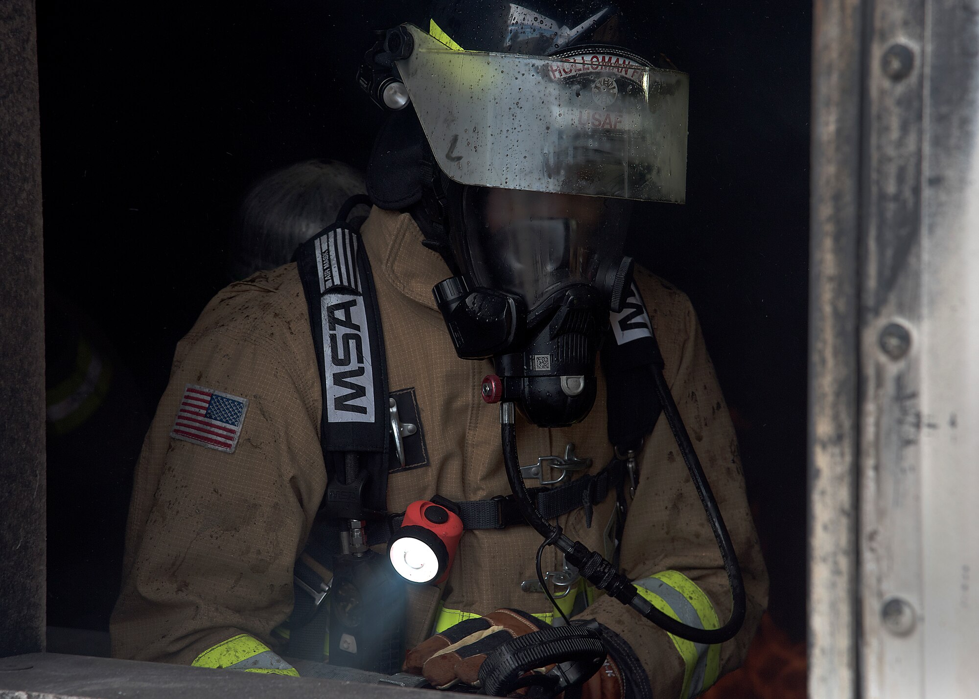 Photo of a firefighter in full gear exiting a building. Smoke is in the background.